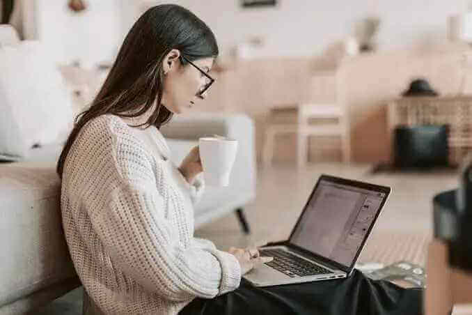 a woman sitting on the floor with a laptop and a cup of coffee